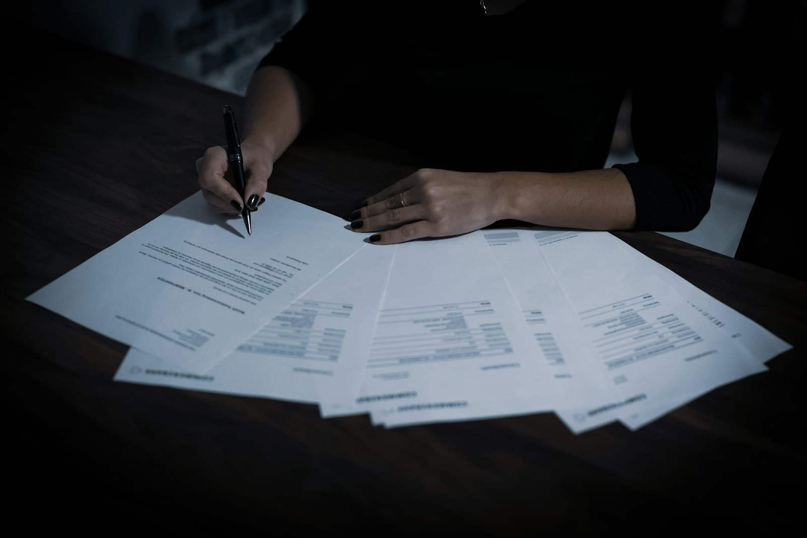 Hands working through a spread of printed statements on a desk at night