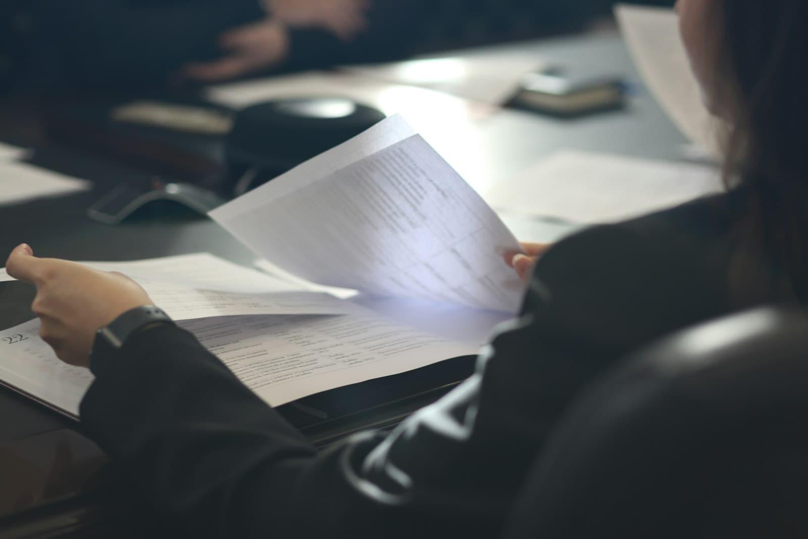 A person in a dark suit reviewing printed documents at a meeting table