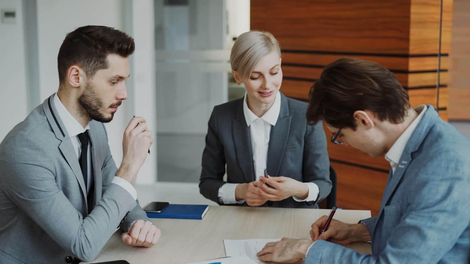 A legal consultation: two advisers at a table while a client signs a document